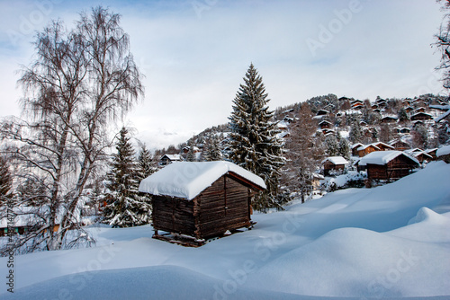 Grange dans un champ de neige avec un village en arrière plan. Station de sports d'hiver dans les Alpes suisses