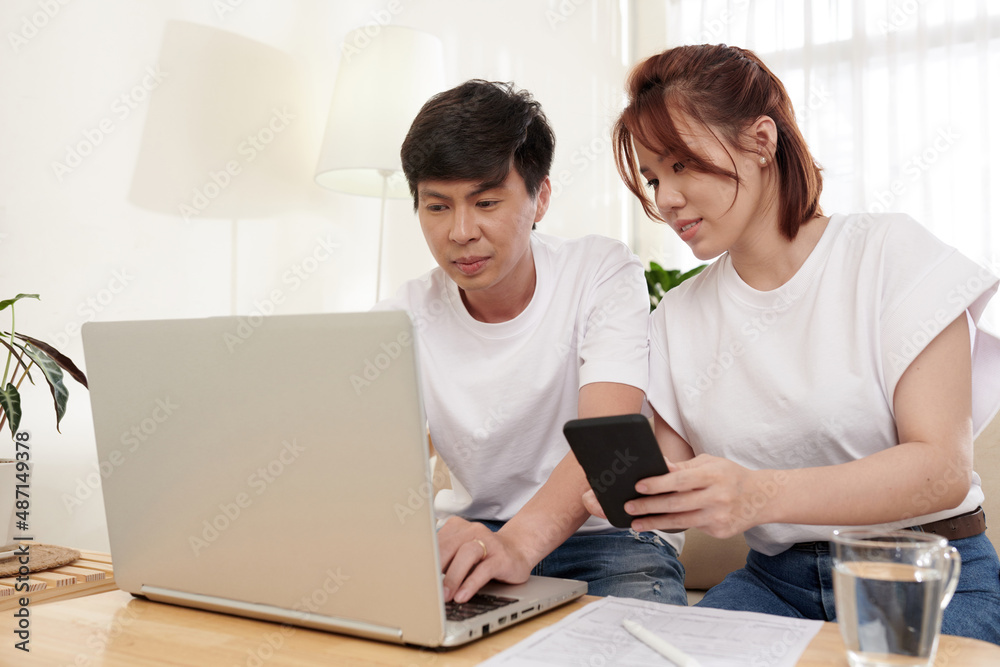 Smiling young husband and wife filling insurance claim form online on laptop and entering personal information Smiling young husband and wife filling insurance claim form online on laptop and entering personal information