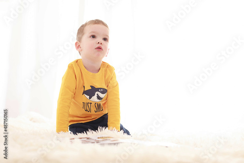 

3 year old baby sitting on a white fluffy blanket in a white room and looking around happily