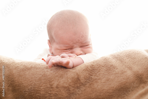 7-day-old newborn rests his head on his hand with half-open eyes sitting on a fluffy brown blanket