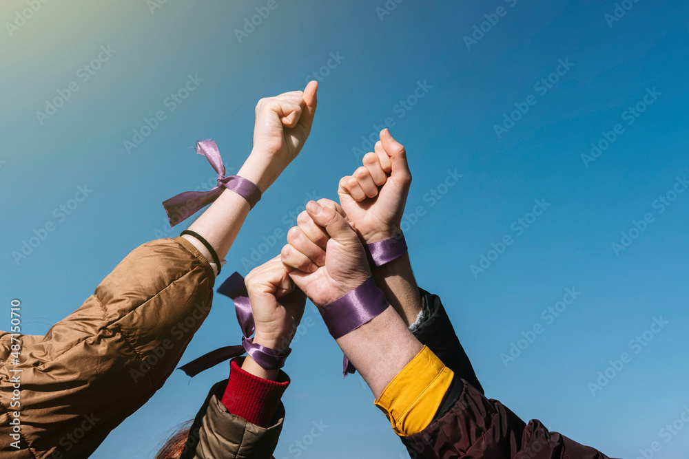 4 women's fists with a purple ribbon on the wrist with the blue sky in the background. Claim concept. Feminist concept. - obrazy, fototapety, plakaty 
