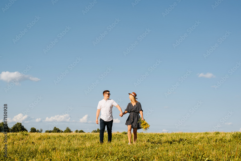 Happy love couple holding hands together and looking at each other on horizon on sunny day, outdoors. Young caucasian heterosexual family romantic trip or walk in nature. Relationship, travel concept