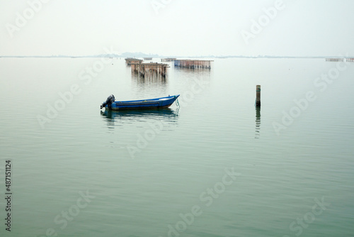 Barca azzurra immersa in atmosfera calma e misteriosa del mare piatto con sfondo allevamenti di vongole e cozze nel mare adriatico presso Chioggia Venezia Italia photo