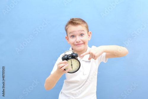 a boy on a blue background with glasses holds an alarm clock in his hands. He woke up, he has a lot of energy