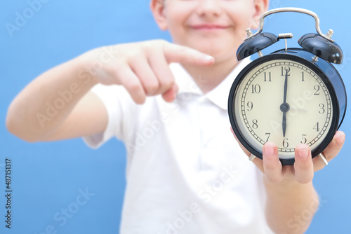 a boy on a blue background with glasses holds an alarm clock in his hands. He woke up, he has a lot of energy