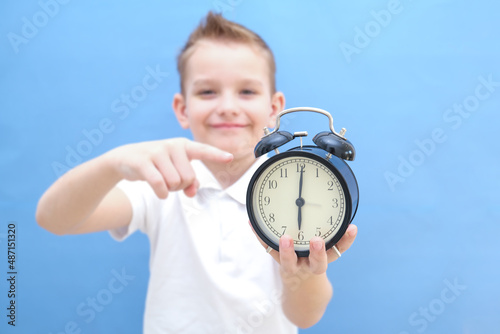 a boy on a blue background with glasses holds an alarm clock in his hands. He woke up, he has a lot of energy