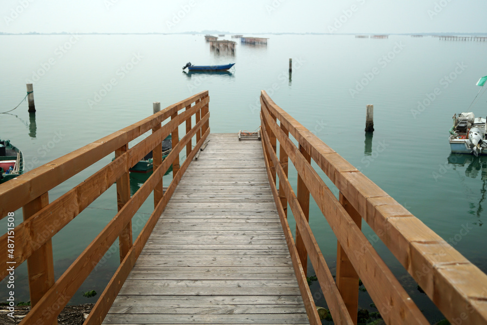 Pontile di legno in prospettiva con vista mare calmo e silenzioso con sfondo di barche e allevamenti di mitili cozze vongole Chioggia Venezia Italia