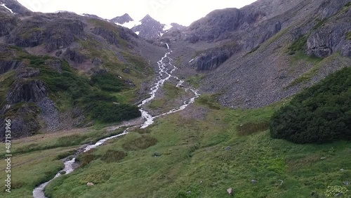 Alpine landscape. Glacier meltdown. Aerial view of a stream flowing downhill across the rocky mountain, green valley and forest during summer in Ushuaia, Tierra del Fuego, Argentina. photo