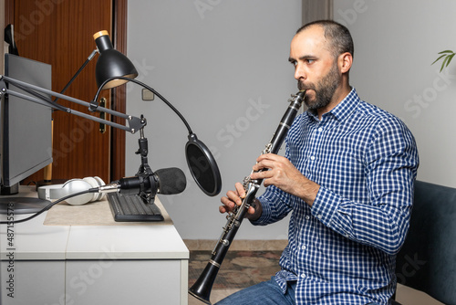 Slika na platnu Young entrepreneur playing the clarinet at home and recording music to stream it