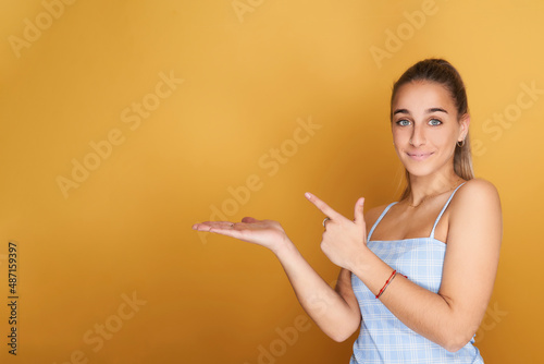 young girl in blue t-shirt pointing to left copy space. Isolated on yellow background