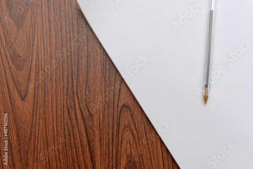 Pen over blank sheet of paper on wooden desk.