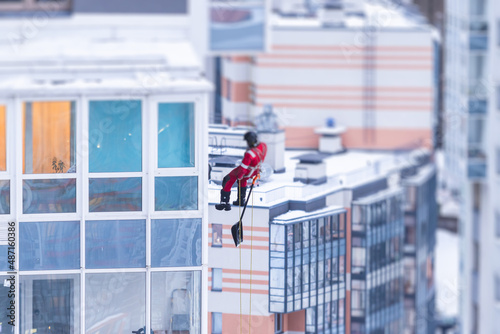 Professional climber rope access worker with a shovel removes snow and take off icicle from high rise building, industrial mountaineers working at heights, manual snow removal, cleaning the roofs © tsuguliev