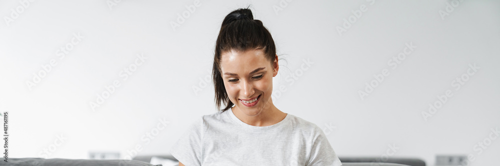 European smiling woman using laptop while sitting on couch at home European smiling woman using laptop while sitting on couch at home