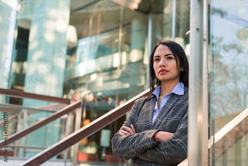 Young businesswoman with her arms crossed looking at the horizon. Glass building in the background.