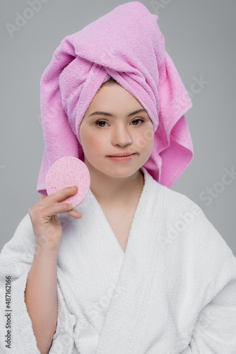 Woman with down syndrome in bathrobe holding sponge isolated on grey