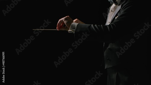 Symphony orchestra conductor wearing suit is directing musicians with movement of baton, isolated on black background. Conducting, directing a musical performance with visible gestures. Close up. photo