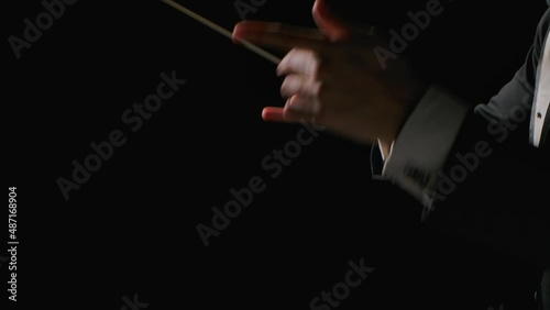 Symphony orchestra conductor wearing suit is directing musicians with movement of baton, isolated on black background. Conducting, directing a musical performance with visible gestures. Close up.