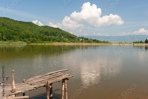 Fish pond at the foot of the mountain, against the blue sky, with a white multicolored cloud approaching.