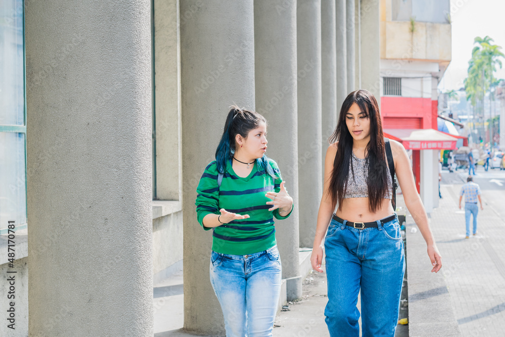 two beautiful latina girls (caucasian and brunette) walking down the street, talking about their studies and discussing their future. concept of education. explaining their thesis.