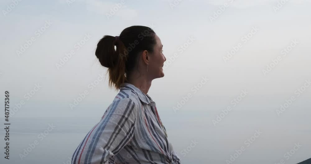 Caucasian independent young girl with brown hair with a pigtail, stands in profile in the shade and looks at the sun. Smiling and happy in braces. Medium shot, slow motion Caucasian independent young girl with brown hair with a pigtail, stands in profile in the shade and looks at the sun. Smiling and happy in braces. Medium shot, slow motion