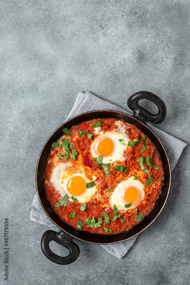 Shakshuka in a frying pan on a gray concrete rustic background. Poached