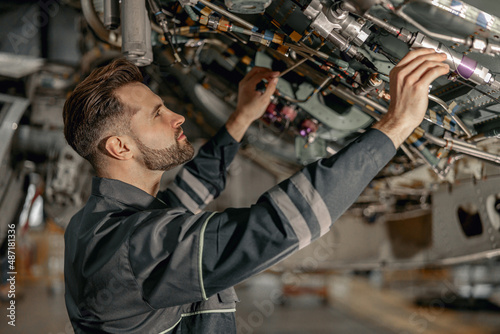 Fotografia Bearded young man aviation mechanic checking aircraft components while working i