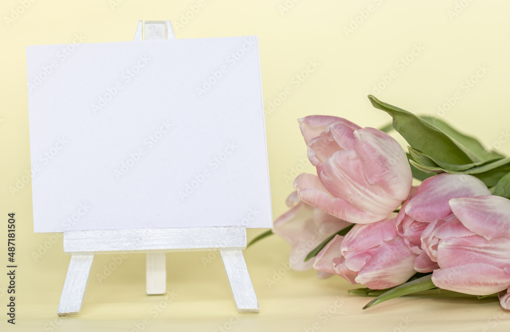 mini easel with blank white paper and some purple tulips by. mother's, woman's day. space for text. hello spring, hello may, sale or greeting. beautiful spring photography. yellow background mini easel with blank white paper and some purple tulips by. mother's, woman's day. space for text. hello spring, hello may, sale or greeting. beautiful spring photography. yellow background