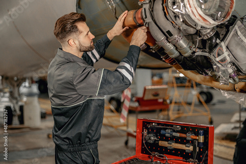 Bearded man maintenance technician tightening bolt with wrench while repairing airplane at repair station photo