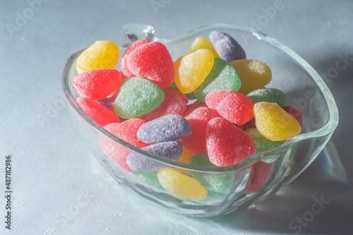 Assorted colorful sweets in a trasparente bowl, light blue background, children's concept and joy
