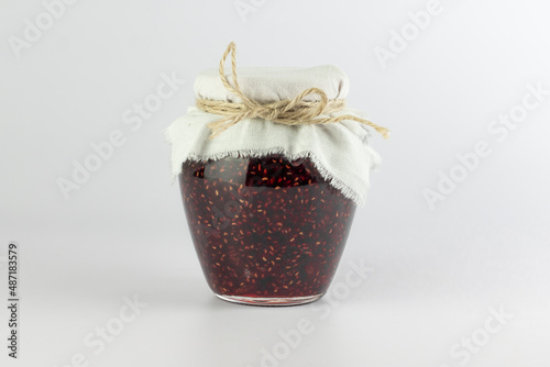 Raspberry jam in glass jar isolated on white background.