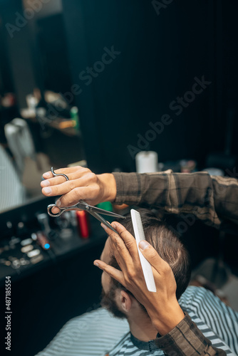 Cheerful young bearded man getting haircut by hairdresser at barbershop