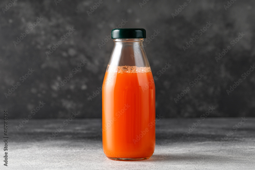 Carrot juice in glass bottle. Freshly squeezed juice on dark background. Mock up, copy space Carrot juice in glass bottle. Freshly squeezed juice on dark background. Mock up, copy space