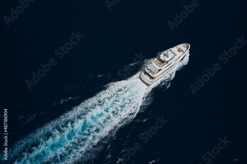 Luxury white mega yacht fast movement on dark water in the ocean top view. Large white super boat moves on the water leaving a white trail on the water aerial view. Big yacht in the sea drone view.