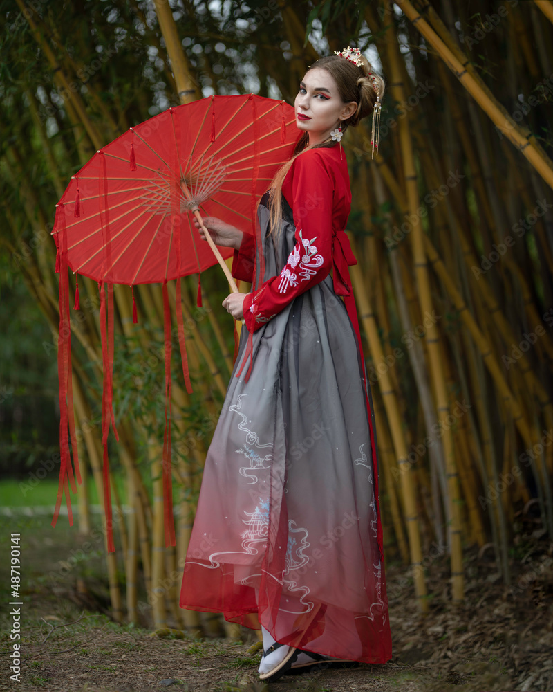 A girl in a national hanbok with a red umbrella with ribbons among yellow bamboo A girl in a national hanbok with a red umbrella with ribbons among yellow bamboo