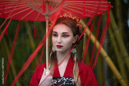 Portrait of a girl in a hanbok with a red umbrella with ribbons on a background of yellow bamboos