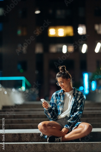 Woman with a smartphone sits on long stone steps in the night city