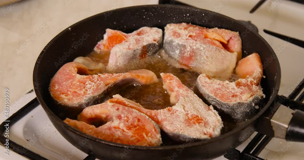 Adding salmon fish in flour into a hot pan with sizzling oil Adding salmon fish in flour into a hot pan with sizzling oil