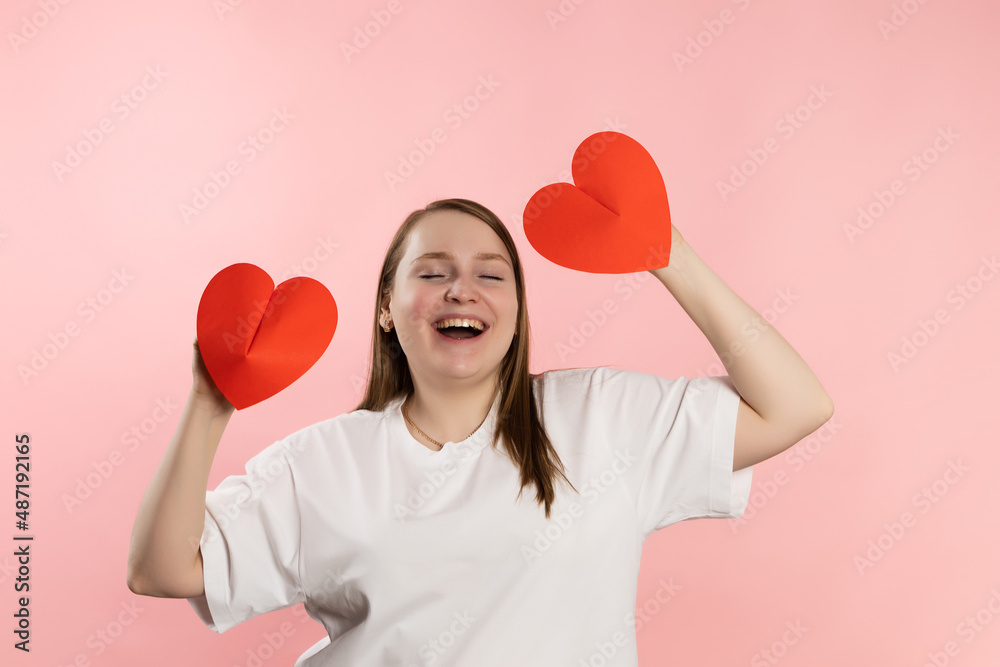 Enjoying young girl with brown hair in a white t-shirt on a pink background and red hearts. High quality photo Enjoying young girl with brown hair in a white t-shirt on a pink background and red hearts. High quality photo