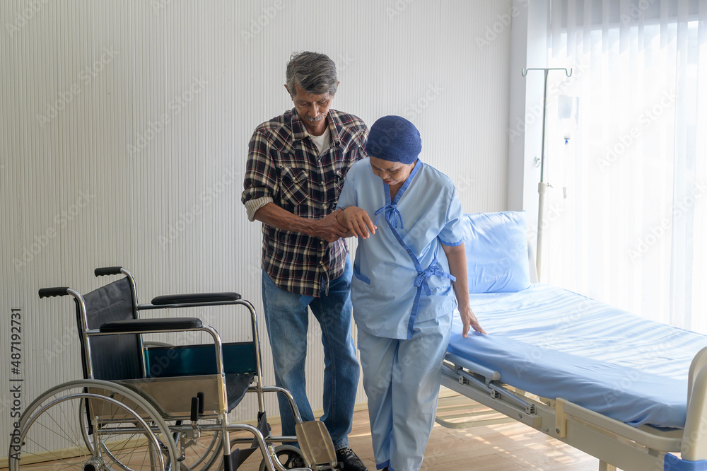 Senior man helping cancer patient woman wearing head scarf moving to wheelchairs at hospital, health care and medical concept