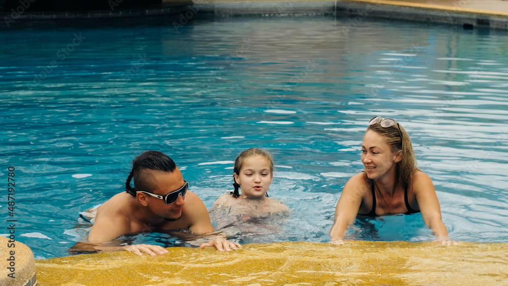 The mother and father with little daughter have fun in the pool. Mom and dad plays with the child. The family enjoy summer vacation in a swimming pool jumping, spinning, splash water. Slow motion. The mother and father with little daughter have fun in the pool. Mom and dad plays with the child. The family enjoy summer vacation in a swimming pool jumping, spinning, splash water. Slow motion.