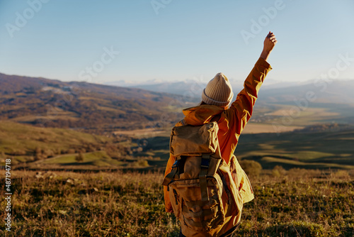 woman in a yellow jacket in a hat backpack travel mountains sunny day