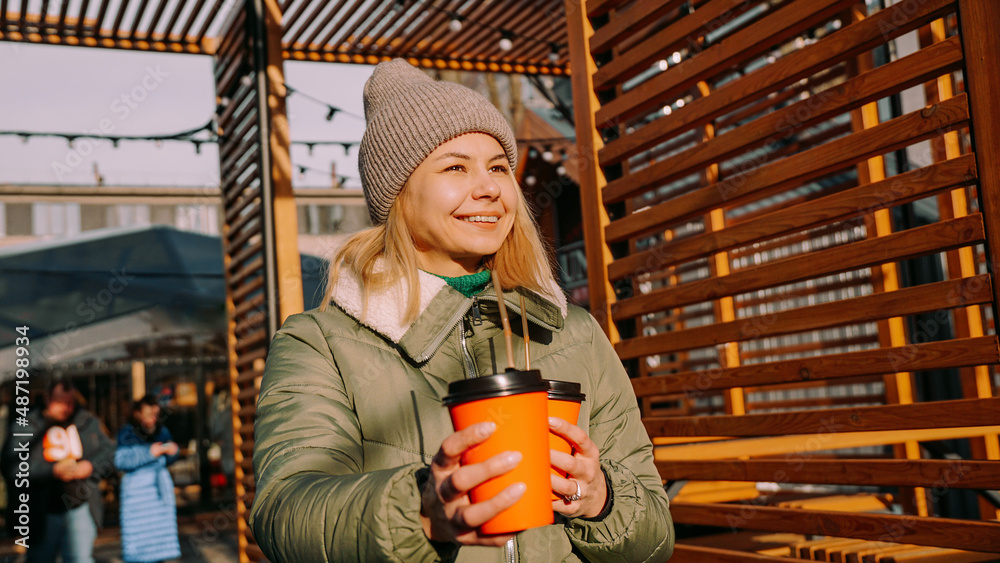 Woman carries two cups of coffee or mulled wine at outside food court. Street food festival, place to relax with friends. She holds the cups forward