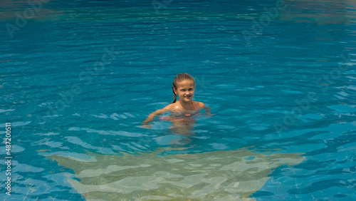 The little cute girl have fun in the swim pool. The child enjoy summer vacation in a swimming pool jumping, spinning, splash water. Slow motion. Happy childhood.