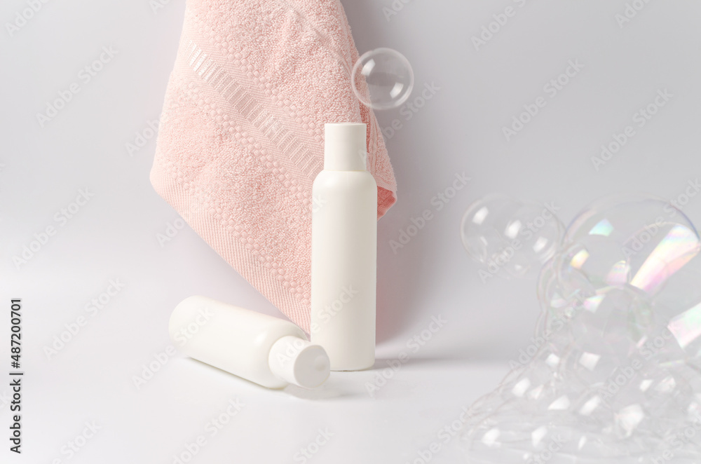 White bottles with gel, shampoo, soap, lotion for skin, hair, face, hands and pink towel on a white background with soap bubbles with selective focus White bottles with gel, shampoo, soap, lotion for skin, hair, face, hands and pink towel on a white background with soap bubbles with selective focus