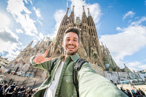 Happy tourist visiting La Sagrada Familia, Barcelona Spain - Smiling man taking a selfie outside on city street - Tourism and vacations concept