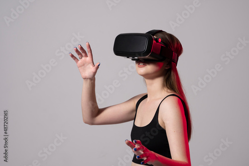 Woman using virtual reality glasses in a studio with a neon light. Business woman wearing VR goggles and interacts with cyberspace using swipe and stretching gestures.