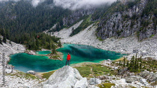 Hiker with a red jacket looks down to the blue glacial Watersprite Lake, Squamish, British Columbia, Canada photo