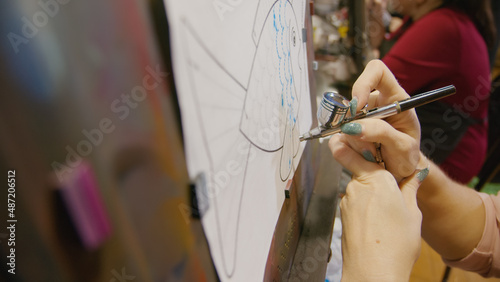 Woman artist learns to paint with airbrush with acrylic dye, paper and easel. Indoors. Concept modern art, airbrushing, aerography, draw spraying picture create sprayer drawing graffiti aerosol spray