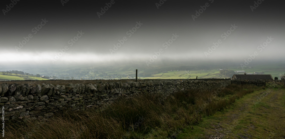 A forbidding landscape of dry stone wall, farmhouse and dark grey sky in the North Pennines, Weardale, County Durham, UK.