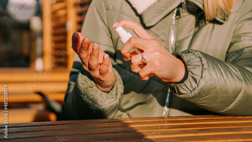 A young woman in a warm jacket treats her hands with an antiseptic outside. Closeup photo